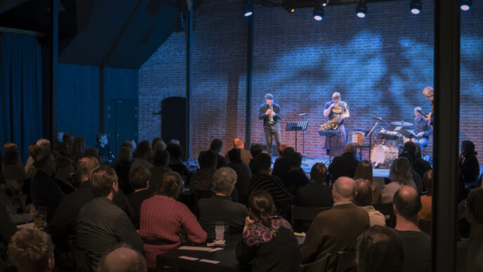 Taka-alalla yhtye esiintymässä Hugo-salin lavalla. Kuvan etualalla paljon yleisöä.