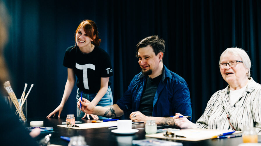 Taidehallin ohjaaja opastaa asiakkaita maalaustyöpajassa.